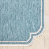 Close-up of Arnola Light Blue Outdoor Rug showing aqua color, woven texture, and cream border detail. Corner
