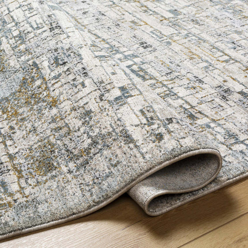 Close-up of the Chaka Textured Rug. Features a contemporary geometric pattern in off-white, gray, blue, and mustard. Fold