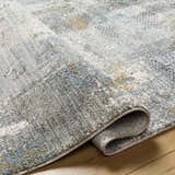 Close-up of the Elina Textured Abstract Rug. The rug has a textured design with dusty sage, ink blue, and mustard accents. Fold