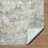 Close-up of Fleur Textured Rug with Fringes. Abstract pattern in gray, light gray, blue and nutmeg. Machine woven polyester rug. Fold