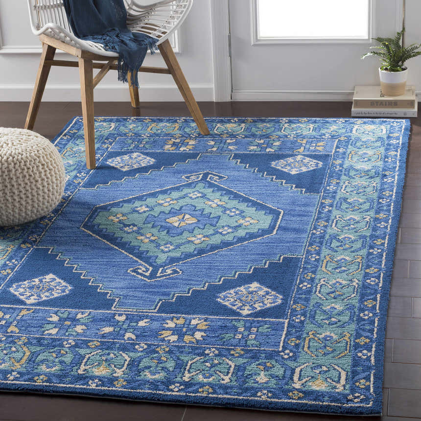 Living room scene with a blue Selden Area Rug, white chair, and knit pouf on dark wood floors. Roomscene-Rectangle