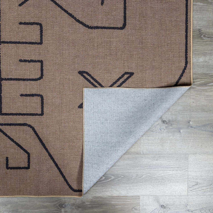 Close-up of the Hamid Washable Jutely Rug in camel with a dark brown geometric pattern and recycled fabric backing. Fold