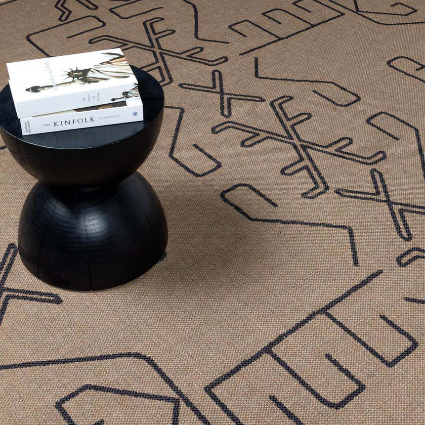 Close-up of the Hamid Washable Jutely Rug in camel with a dark brown geometric pattern and a black accent table. Styleshot