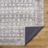 Close-up of the Mabyn Area Rug showing its traditional design, neutral colors, and machine-woven texture on a wood floor. Fold