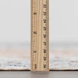 Close-up of the Emke Flat Pile Washable Rug showing the rug's pile height with a ruler. Bone, beige, and gray tones. Pile