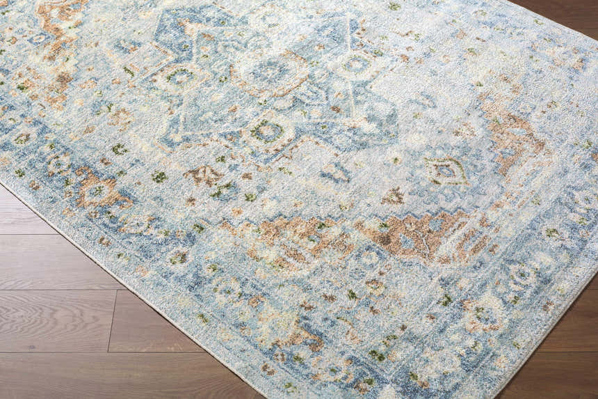Close-up of the Ezri Washable Area Rug. Beige, light blue, and orange farmhouse-style rug with a traditional pattern. Corner