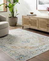 Living room scene with Ezri Washable Area Rug in beige, light blue, and orange. Farmhouse style with wood cabinet and neutral armchair. Roomscene-Rectangle