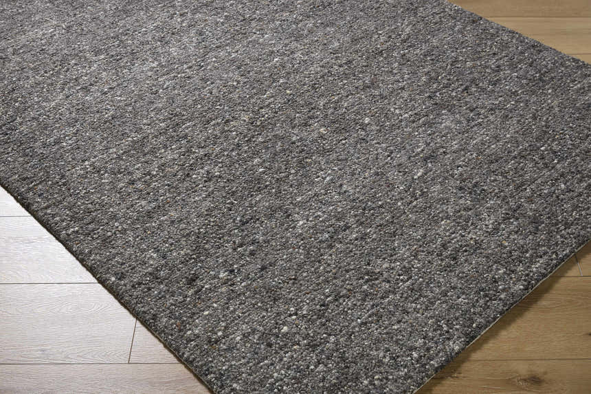 Close-up of the hand-tufted Sevan Black Wool Area Rug. Shows the rug's texture and color variations of jet black, gray, and taupe. Corner