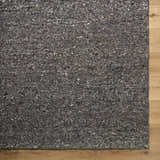 Close-up of the textured Sevan Black Wool Area Rug with jet black, medium gray, and taupe tones on wood floor. Corner