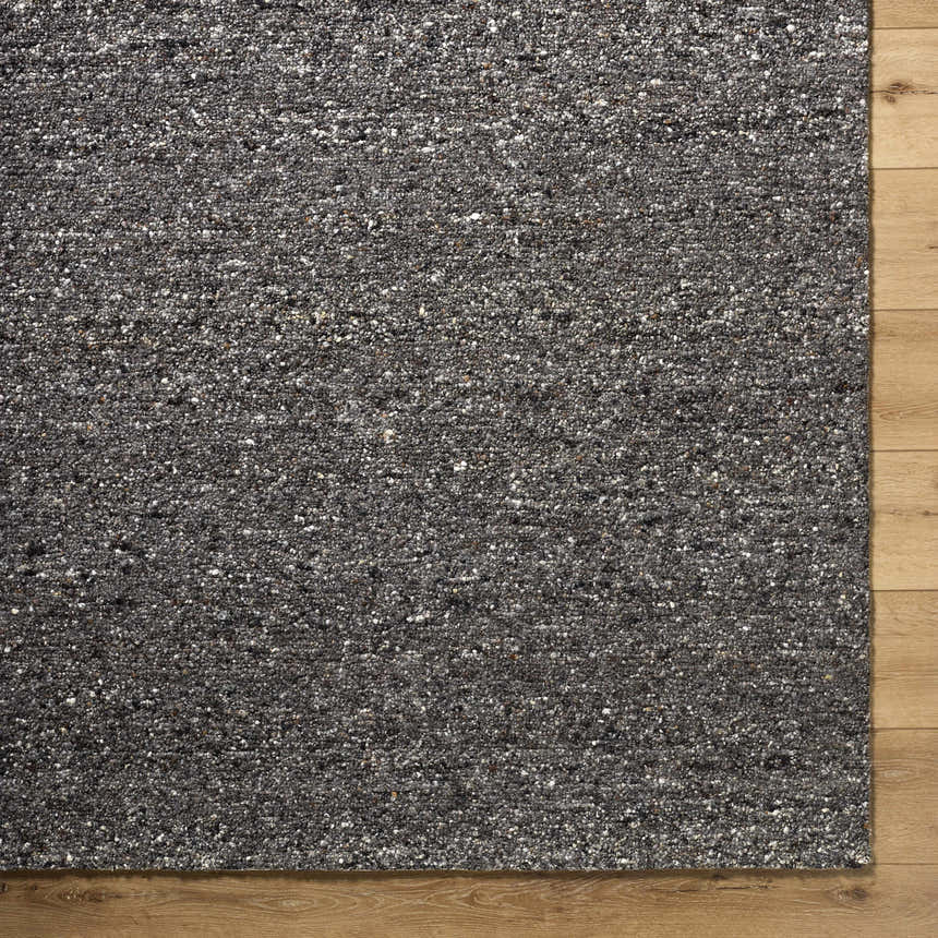 Close-up of the textured Sevan Black Wool Area Rug with jet black, medium gray, and taupe tones on wood floor. Corner