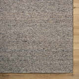 Close-up of the textured Sevan Taupe Wool Area Rug. Neutral colors with dark flecks. Farmhouse style rug on light wood floor. Corner