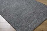 Close-up of the hand-tufted Sevan Charcoal Wool Area Rug. The rug has a textured look with shades of gray and black. Corner