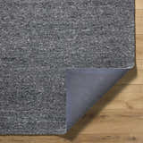 Close-up of the hand-tufted Sevan Charcoal Wool Area Rug showing its gray tones and cotton backing on a wood floor. Fold