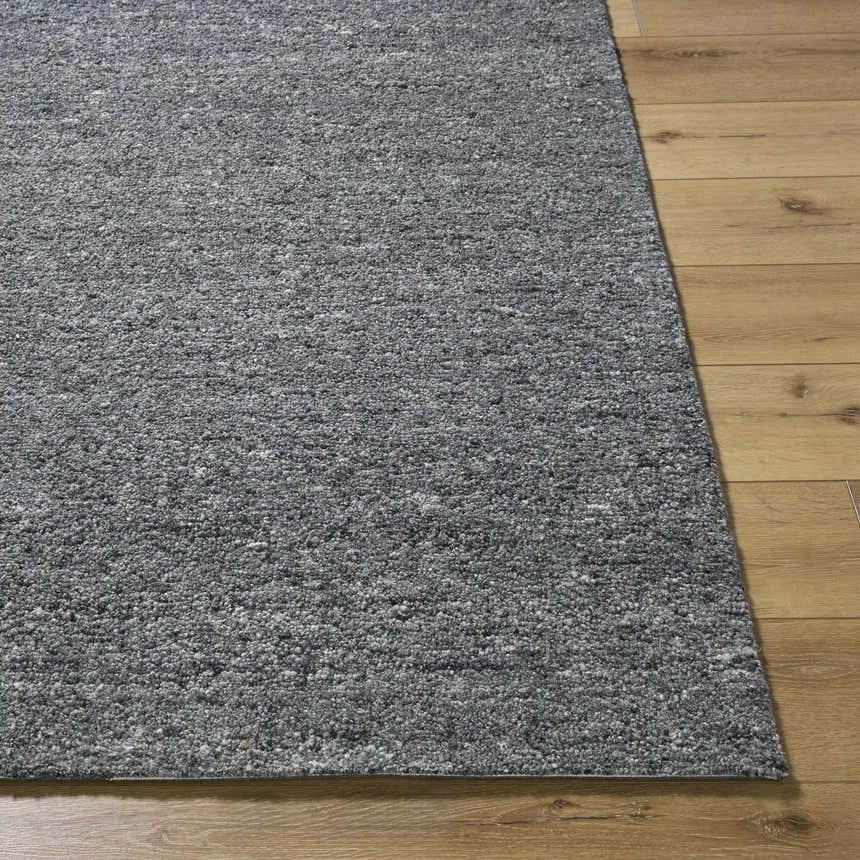 Close-up of the hand-tufted Sevan Charcoal Wool Area Rug showing its gray tones and textured wool fibers on wood floor. Front