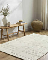 Minimalist room scene with a light wood bench and the off white Fusao area rug with geometric pattern. Roomscene-Rectangle