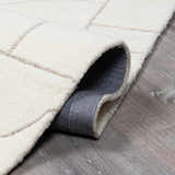 Close-up of a hand-tufted Fusao Off White Area Rug showing wool texture and geometric pattern on gray wood floor. Fold