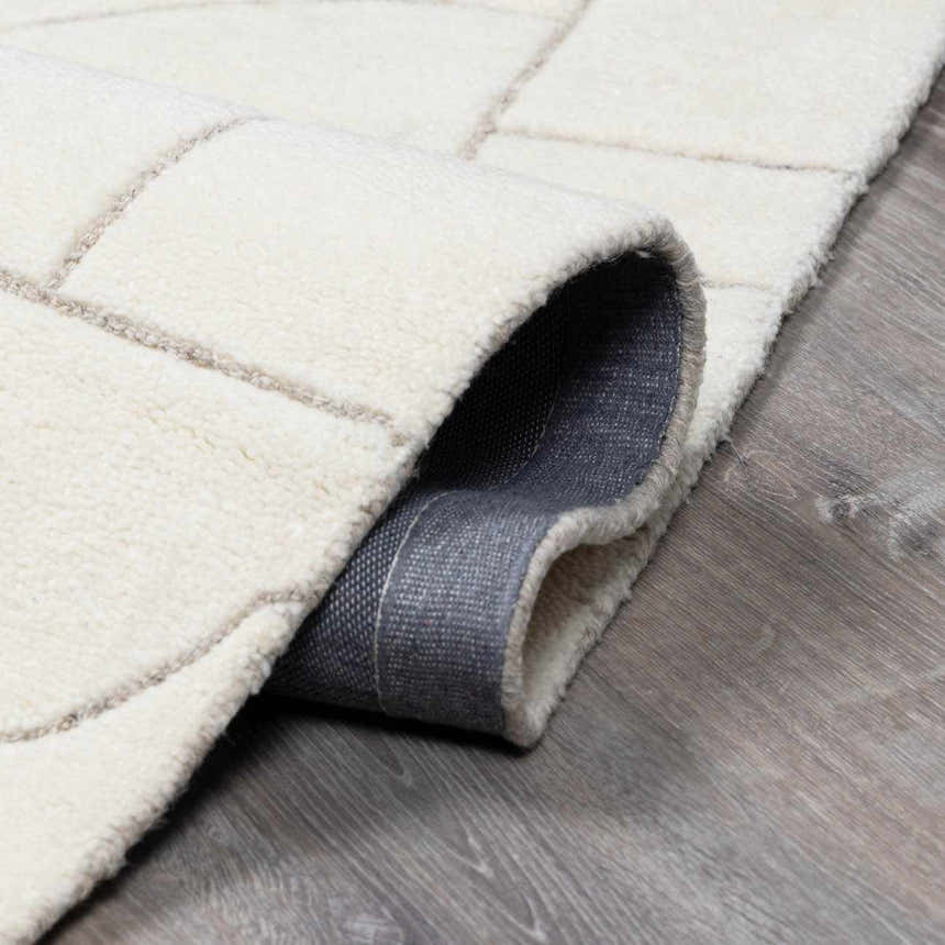 Close-up of a hand-tufted Fusao Off White Area Rug showing wool texture and geometric pattern on gray wood floor. Fold