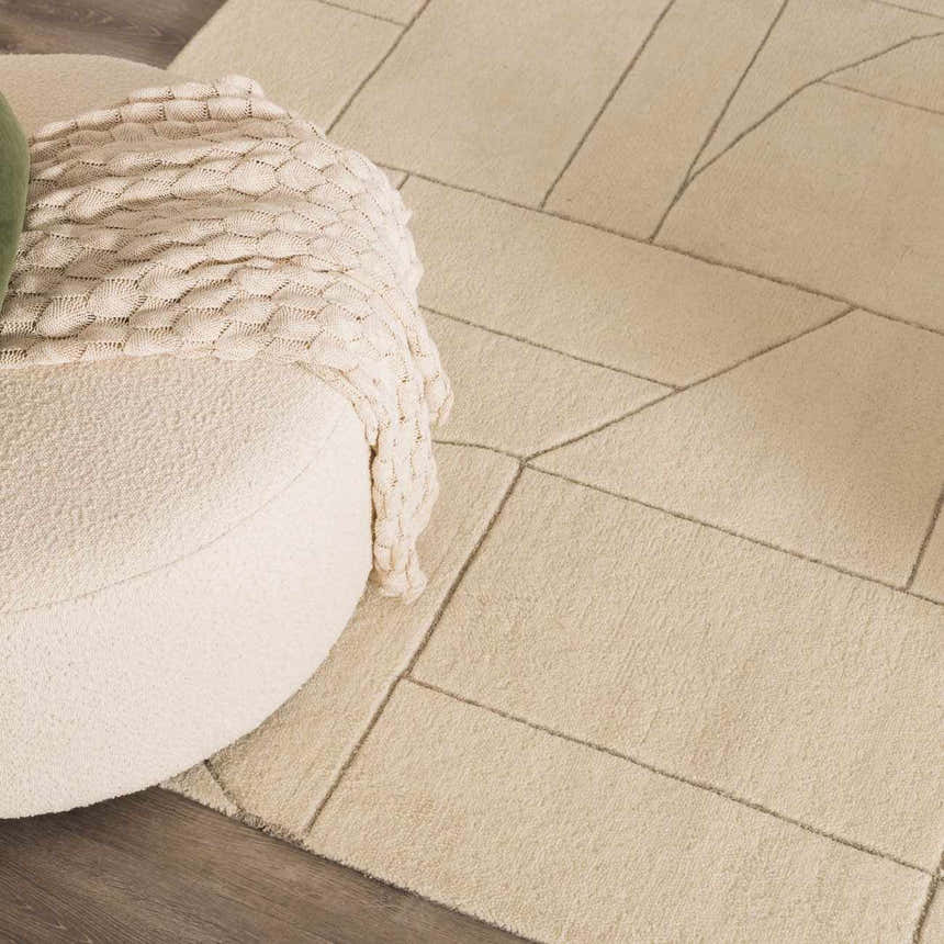 Close-up of the textured, off-white Fusao Area Rug with a geometric pattern and a cozy ottoman with a knitted throw. Roomscene-Rectangle