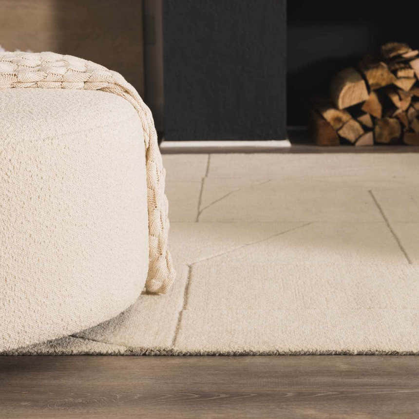 Close up of the textured, off white Fusao Area Rug with geometric design next to a cream ottoman. Roomscene-Rectangle