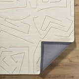 Close-up of the hand-tufted Mony Beige Area Rug. Features a geometric beige pattern on a soft, textured, cream-colored wool. Fold