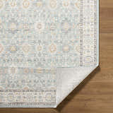 Close-up of Adilet Blue Washable Area Rug on wood floor. Farmhouse style with traditional floral pattern in blue, gold, and gray. Fold