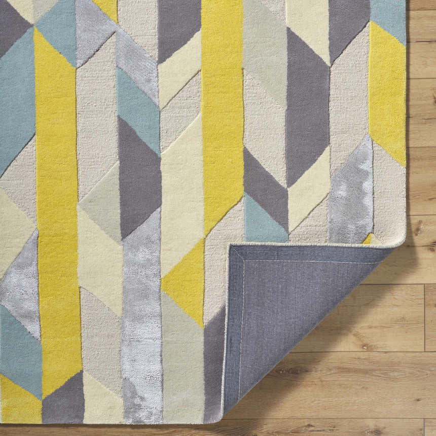 Close-up of the Zoie Area Rug showing its geometric design in camel, gray, lambswool, and yellow tones. Hand-tufted wool texture. Fold