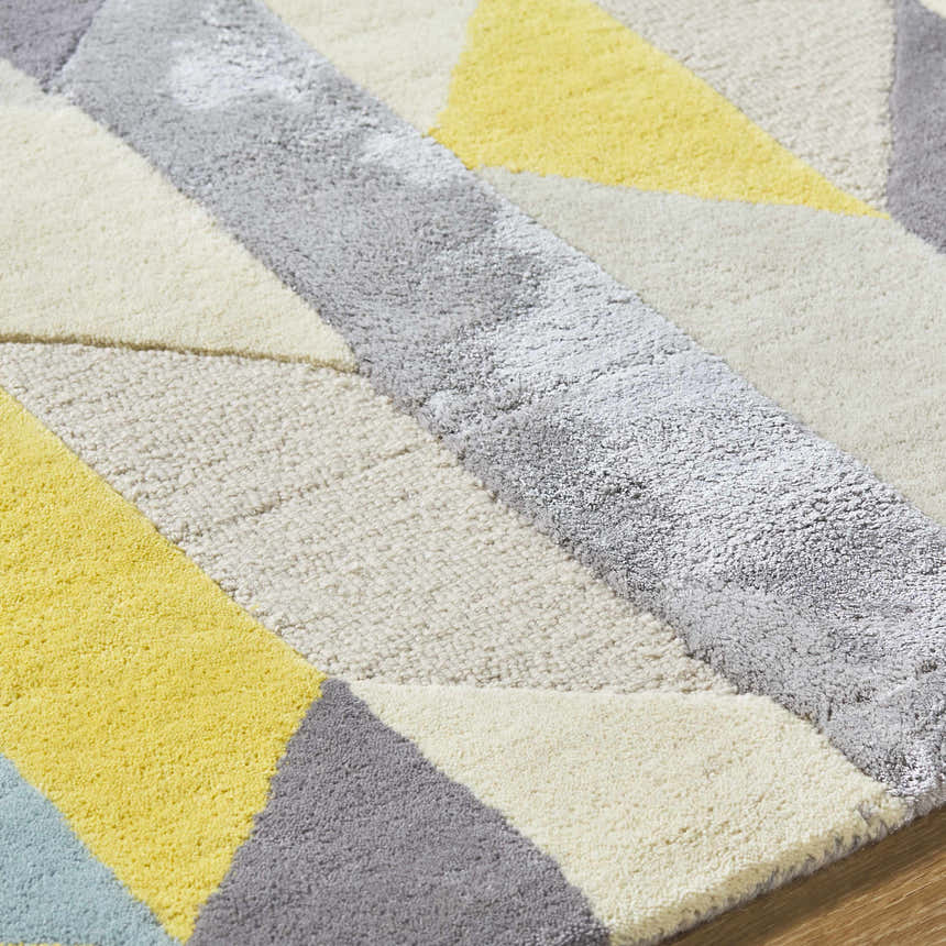 Close-up of the hand-tufted Zoie Area Rug. Features a geometric pattern in camel, gray, lambswool, and saffron hues. 70% wool. Texture