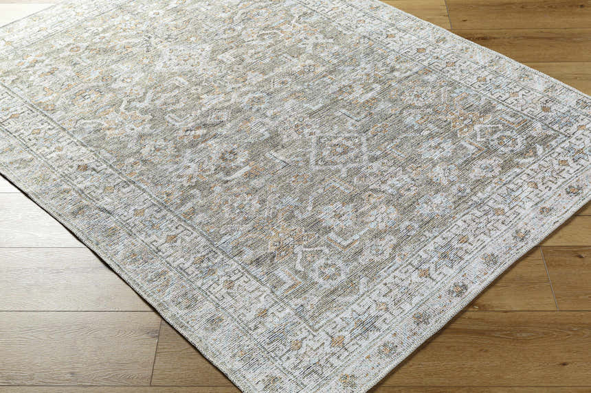 Close-up of the Tisha Washable Area Rug. Farmhouse style rug in gray, tan, and silver with a traditional design and border. Corner