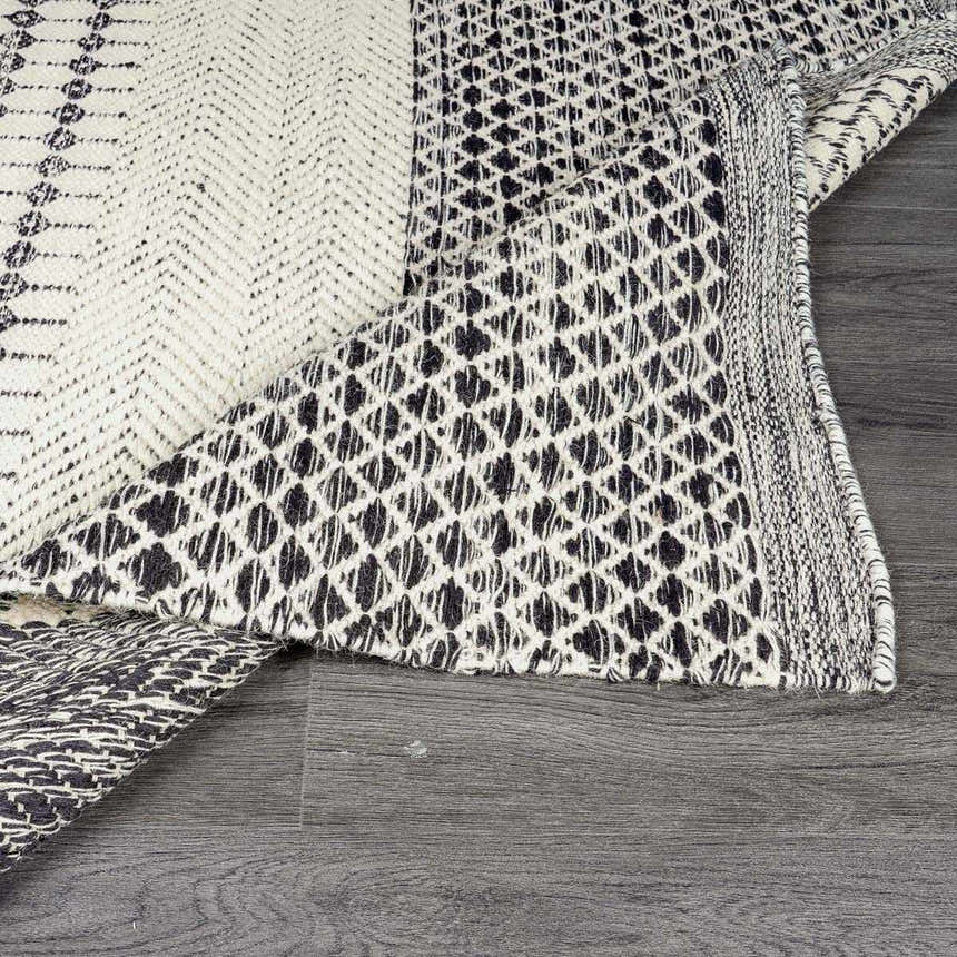 Close-up of the hand woven Tideswell Scandi Boho Wool Carpet with beige and black geometric patterns and fringe. Fold