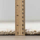 Close-up of the Teige Light Silver Area Rug showing its thick, hand-tufted wool pile height with a ruler. Pile