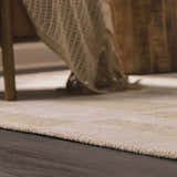 Close-up of the textured Teige Light Silver Area Rug on dark wood floor, with a throw blanket and chair leg. Styleshot