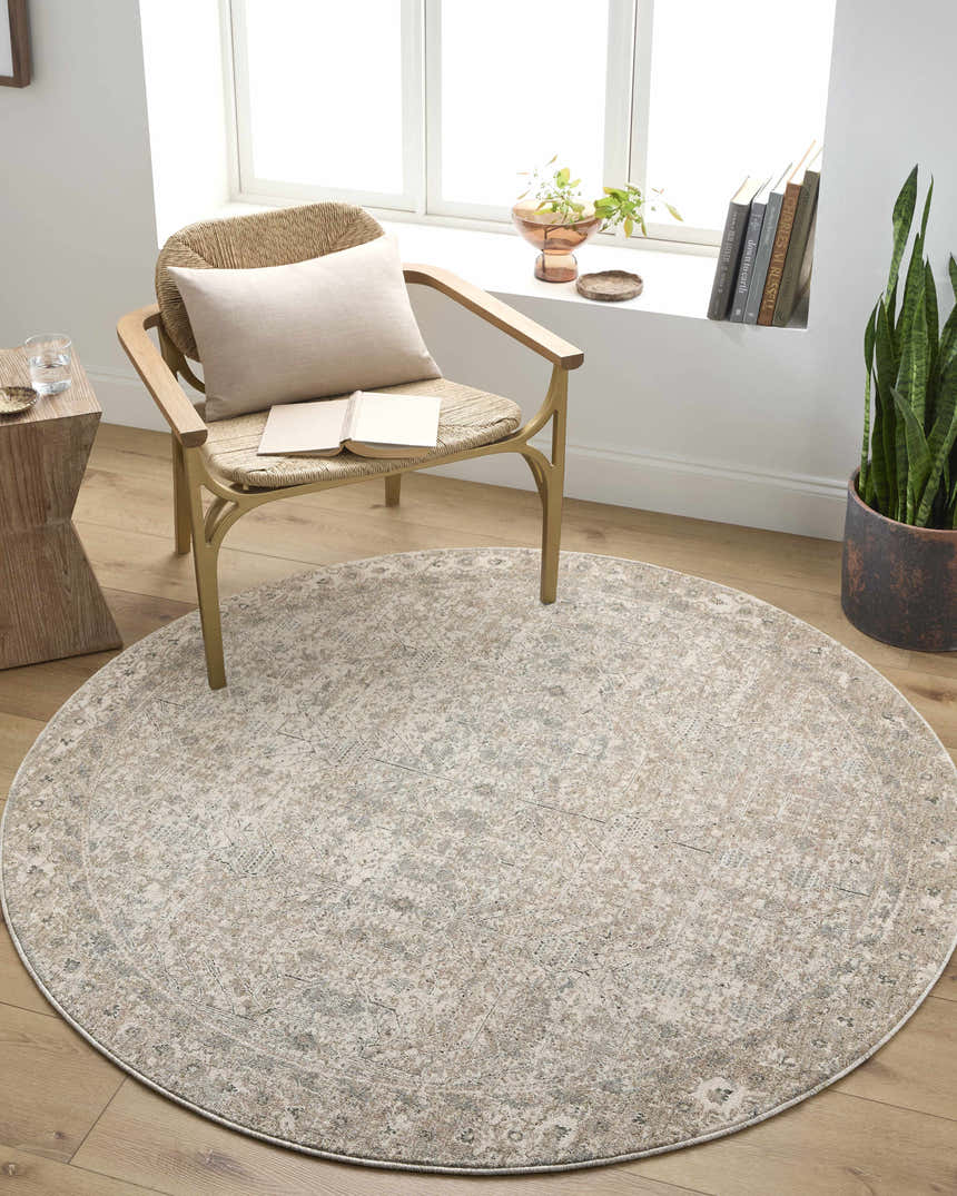 Light-filled room scene with a round Avalyn Area Rug in cream, sage, and tan under a chair with a book. Roomscene-Round