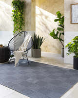 Modern patio scene with Veras Charcoal Area Rug, black chair, and potted plants. Roomscene-Rectangle