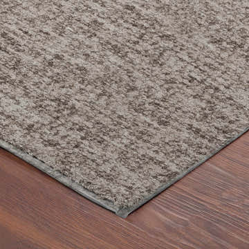 Close-up of the textured Dalyn Luxury Voyage VY2 Taupe Washable Area Rug on a wood floor. Ivory and taupe tones.