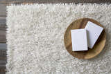 Close-up of the Browder Solid Beige Shag Area Rug showing its plush texture. Wooden tray and books are styled on the rug. Styleshot