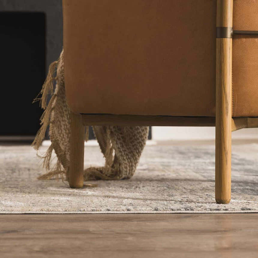 Living room scene featuring a Whyalla Misty Thick Luxe Rug under a tan leather chair with a fringed throw blanket. Styleshot