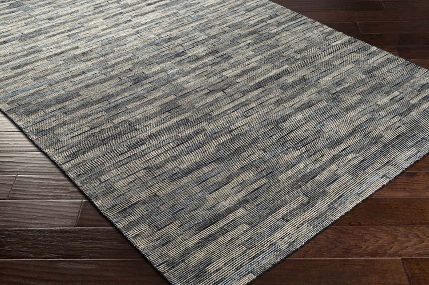 Close-up of the hand-knotted Willmar Premium Rug. Denim, ink blue, and light olive stripes on a textured wool rug. Corner