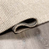 Close-up of the Wolseth Area Rug showing its hand woven texture, off white color, and durable wool and polyester material. Fold