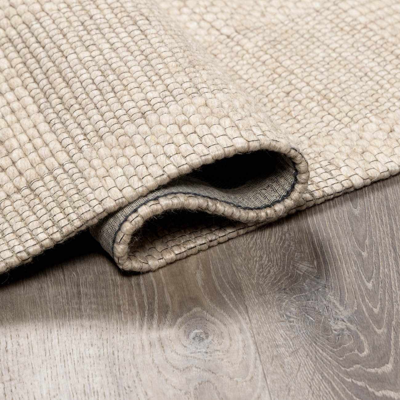 Close-up of the Wolseth Area Rug showing its hand woven texture, off white color, and durable wool and polyester material. Fold