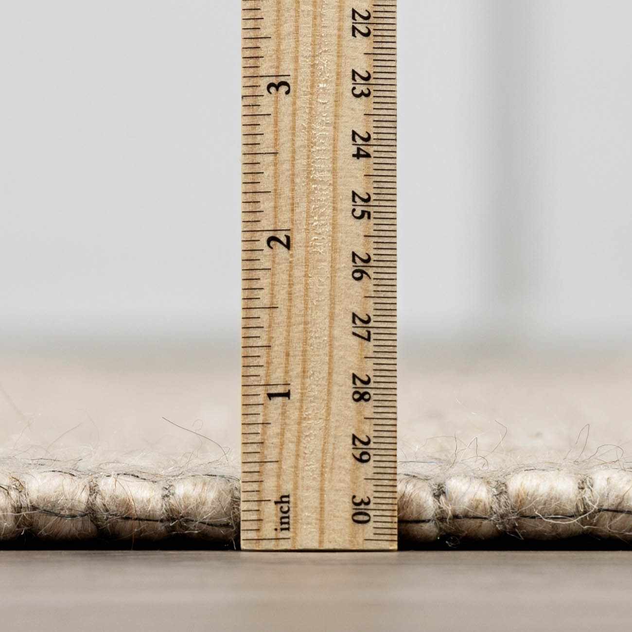 Close-up of the Wolseth Area Rug showing the pile height with a ruler. Off white wool and polyester texture. Pile