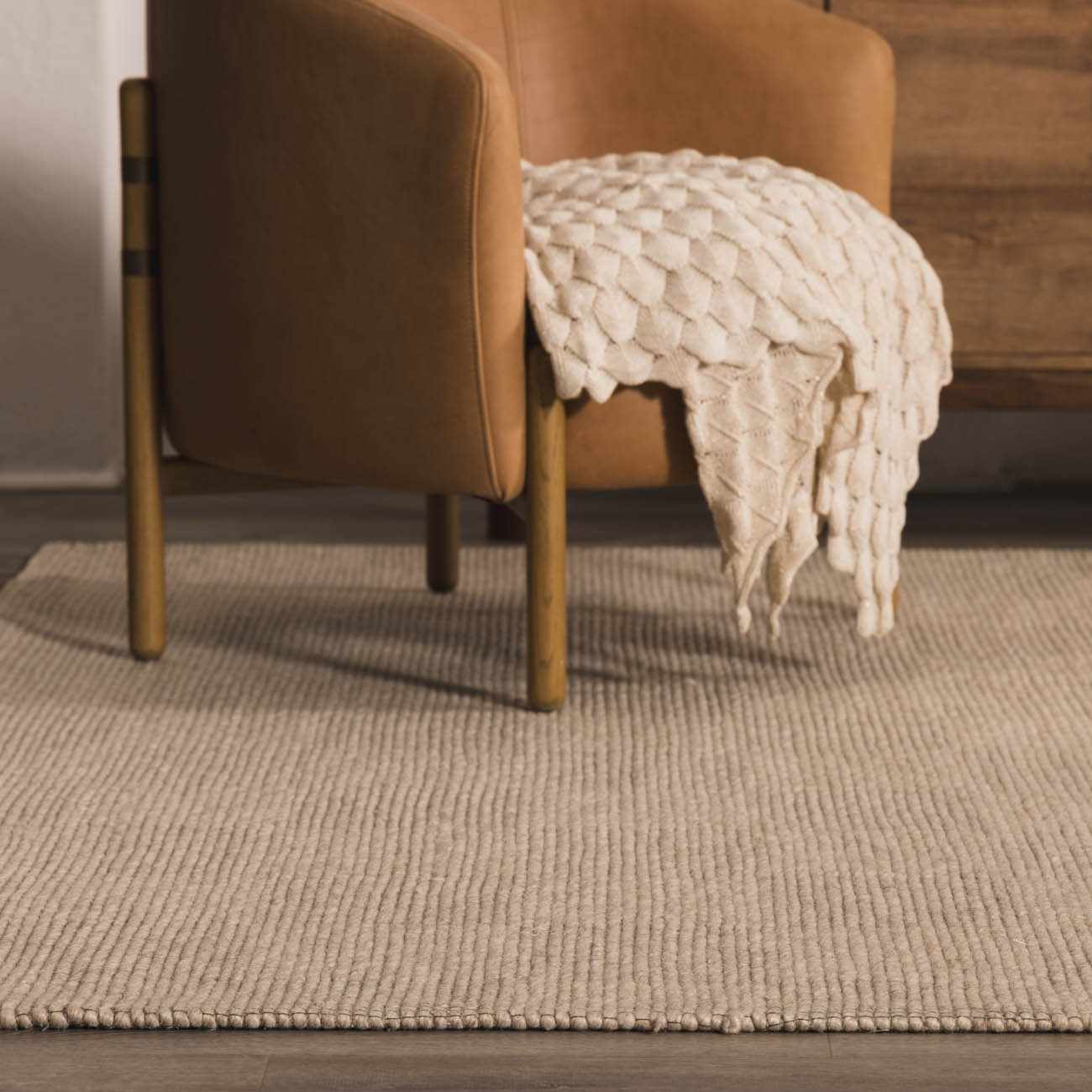 Living room scene with a tan leather chair on the Wolseth Area Rug. The rug is off-white with a subtle ribbed texture. Roomscene-Rectangle