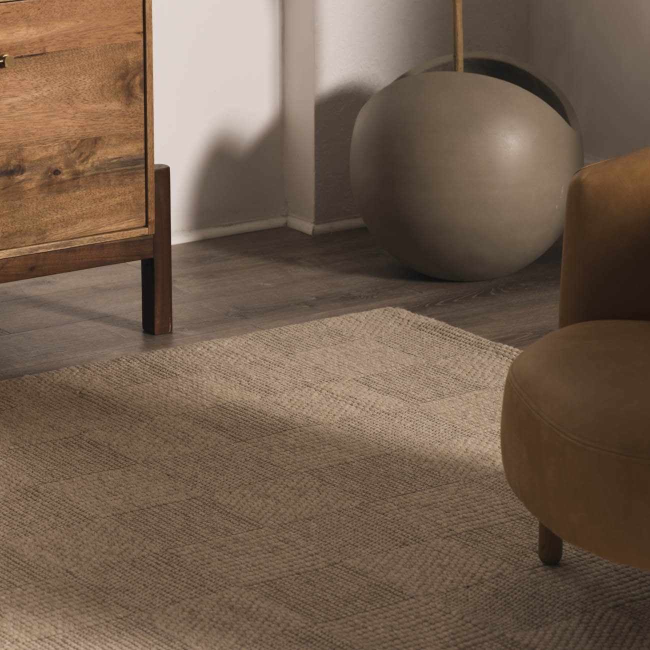 Close-up of the Wolseth Area Rug showing its textured, woven design in neutral tones, styled with wood furniture. Styleshot