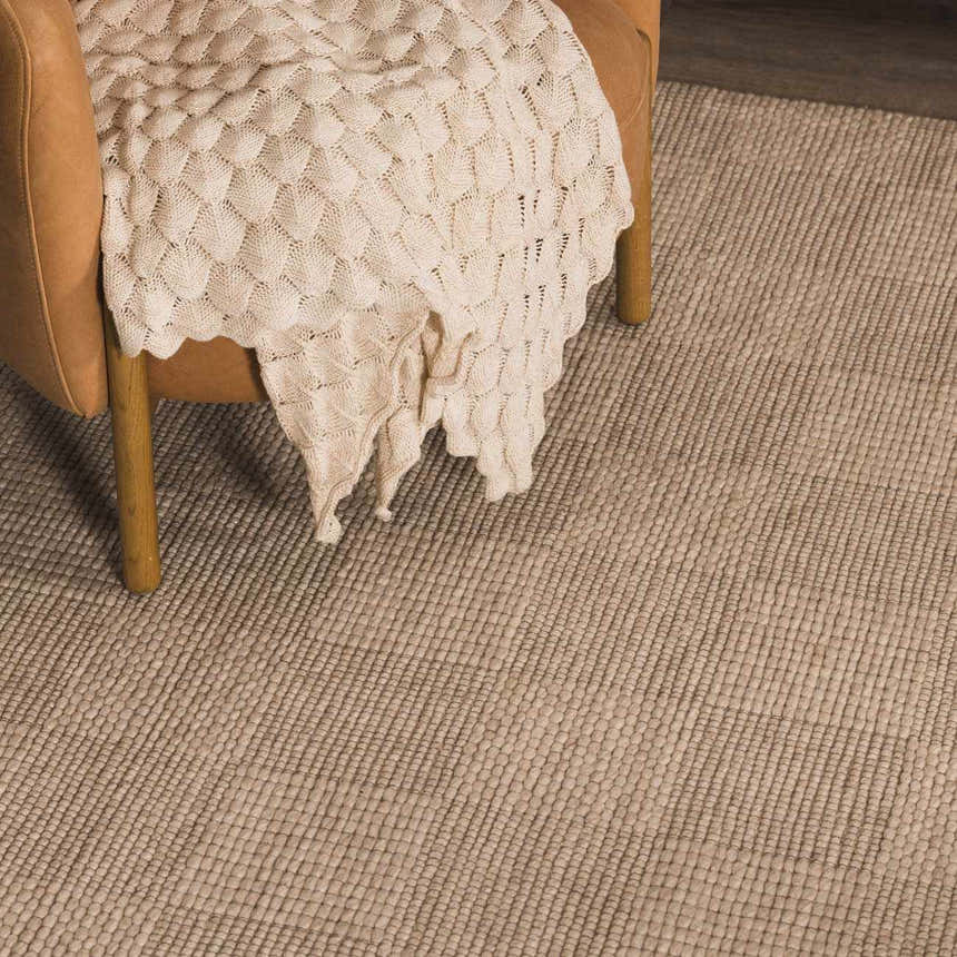 Close-up of the hand woven Wolseth Area Rug in off white, showing texture and a chair with a blanket. Styleshot