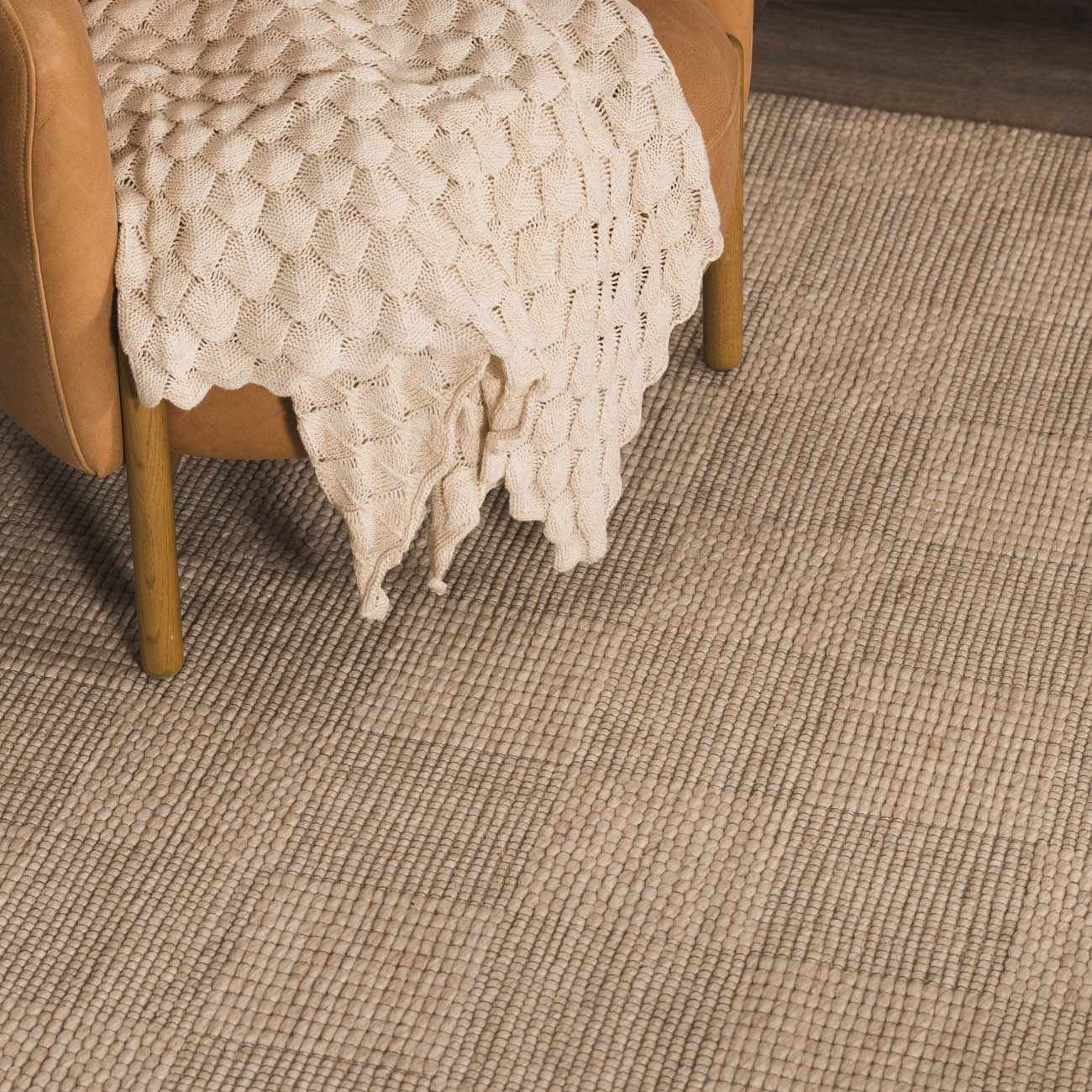 Close-up of the hand woven Wolseth Area Rug in off white, showing texture and a chair with a blanket. Styleshot