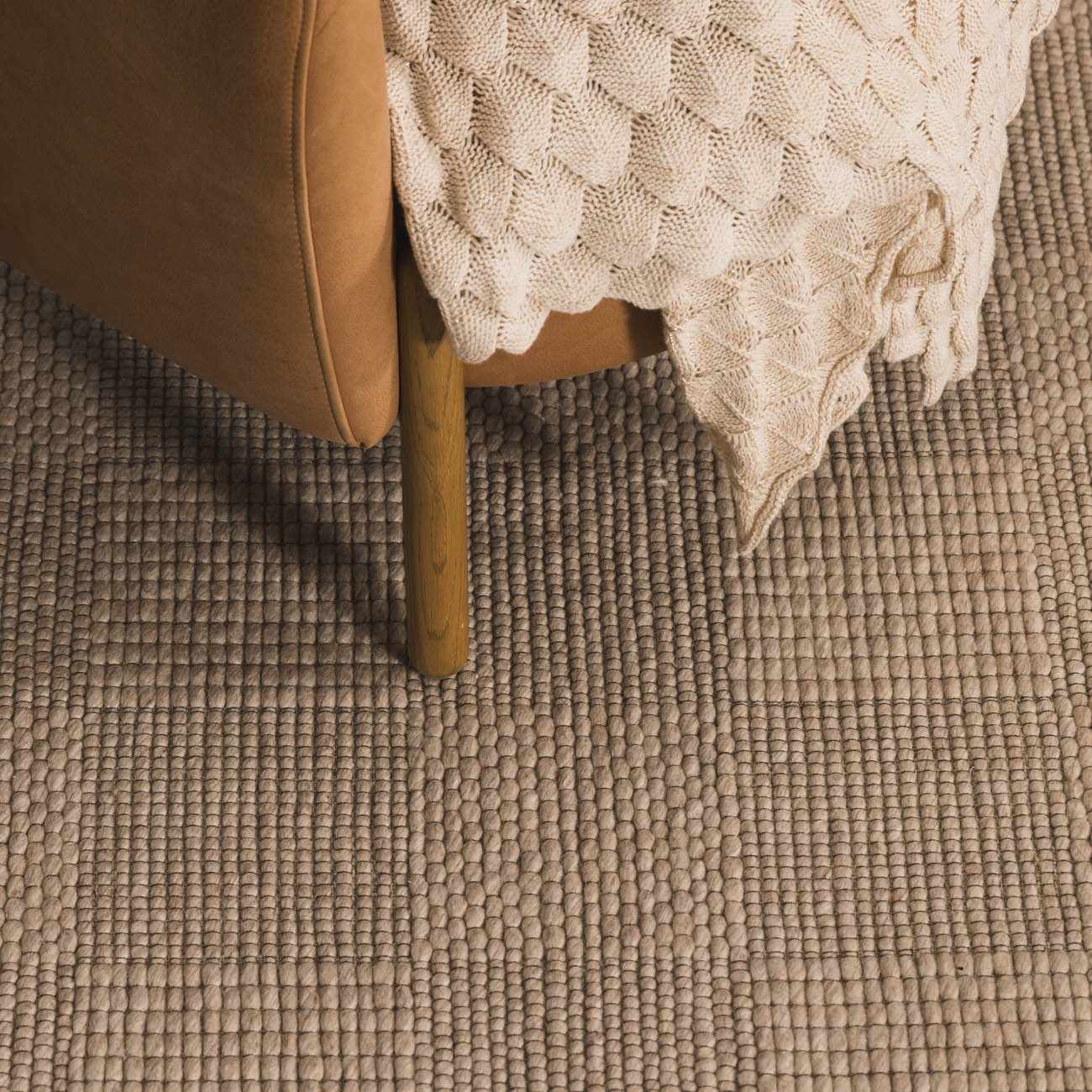 Close-up of the Wolseth Area Rug showing its ivory woven texture next to a tan chair and a cozy knit blanket. Roomscene-Rectangle