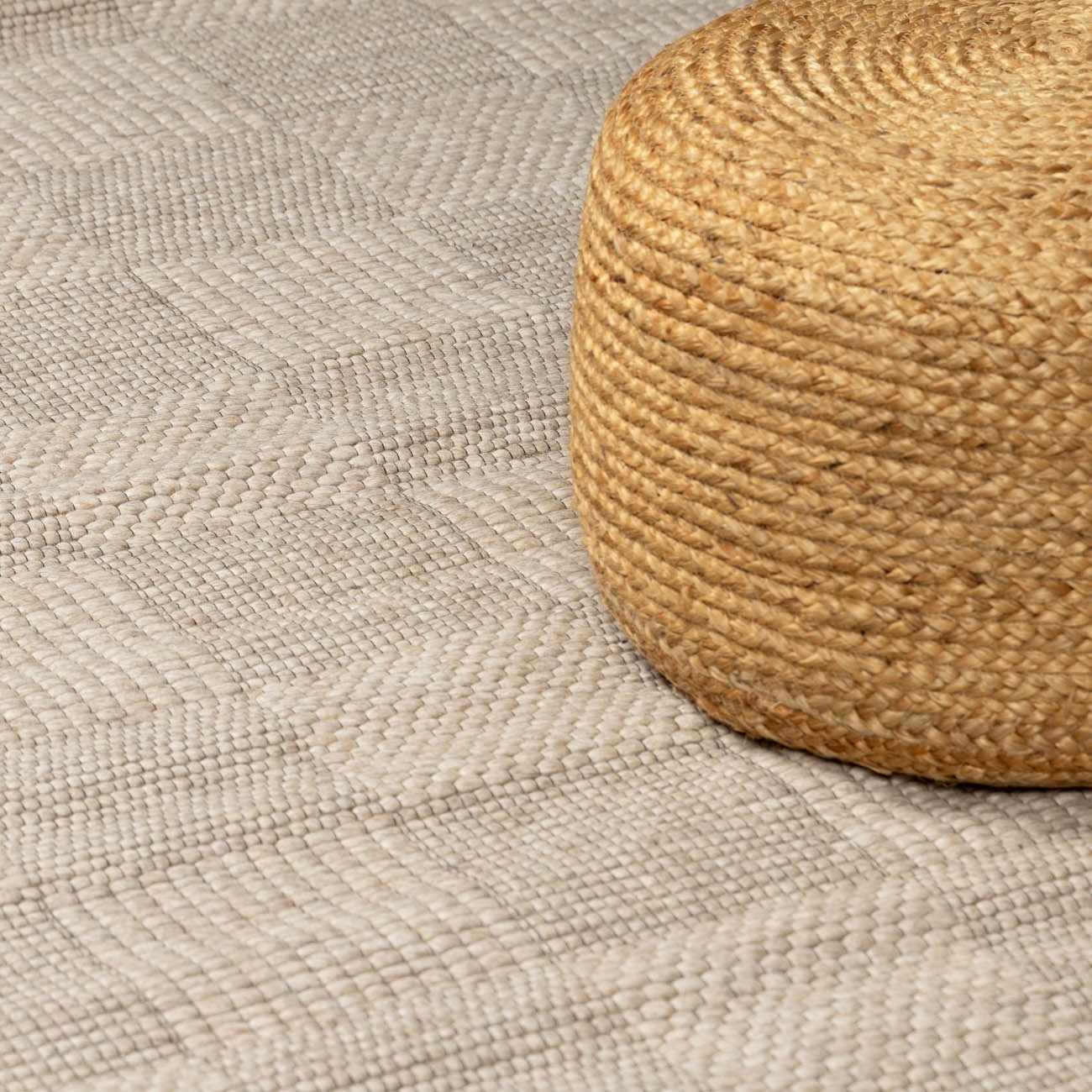 Close-up of the ivory Wolseth Area Rug showing its hand-woven texture and subtle herringbone pattern, paired with a jute pouf. Styleshot