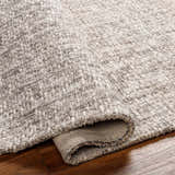 Close-up of the textured Westoning Area Rug. Hand-loomed polyester rug in off-white, light gray, and charcoal on a wood floor. Fold