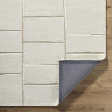 Close-up of the hand-tufted Xylia Beige Area Rug. Off-white wool rug with a light silver geometric pattern. Fold