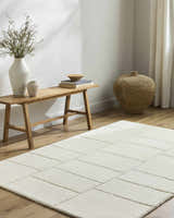 Neutral room scene with a light beige Xylia wool rug, wood bench, vases, and woven basket for a minimalist aesthetic. Roomscene-Rectangle