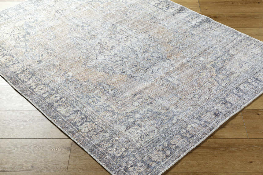 Close-up of the Yachi Washable Area Rug. Farmhouse style rug in gray, silver, and prairie dust colors. Machine woven texture. Corner